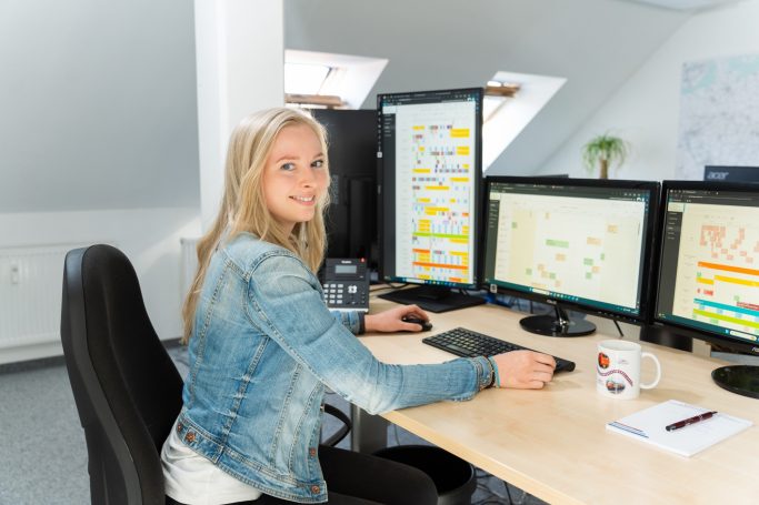 Frau sitzt an einem Schreibtisch mit mehreren Monitoren und arbeitet am Computer.